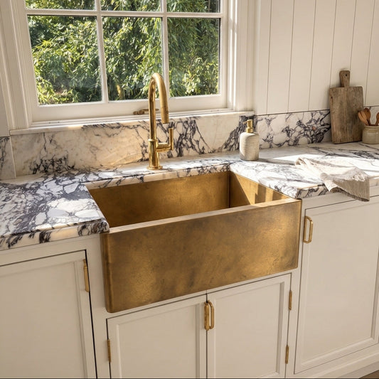 Natural brass farmhouse sink in marble countertop with brass faucet and cream cabinets, handcrafted in the USA