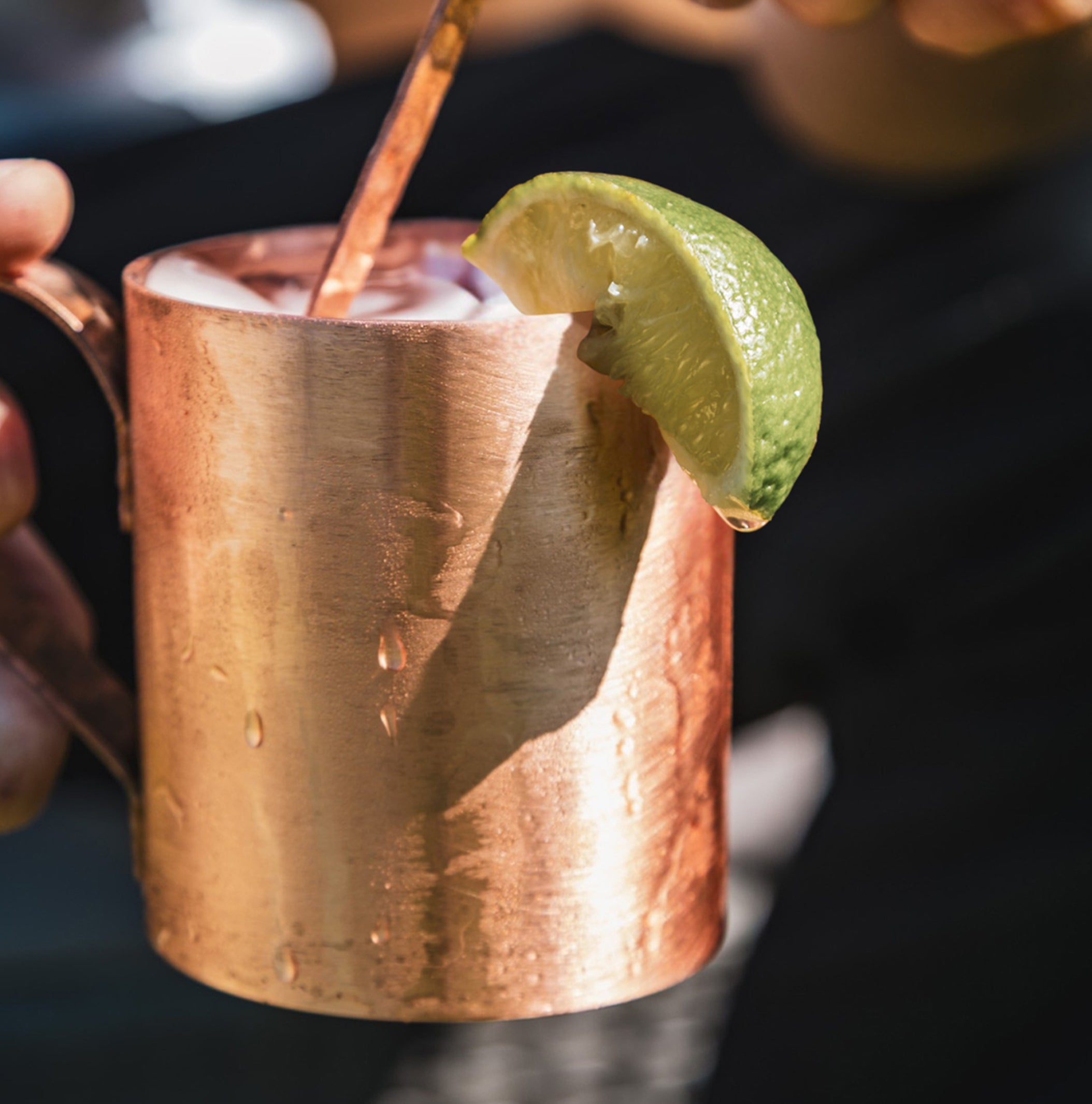 Copper mug with a cocktail and lime wedge, held by a hand.