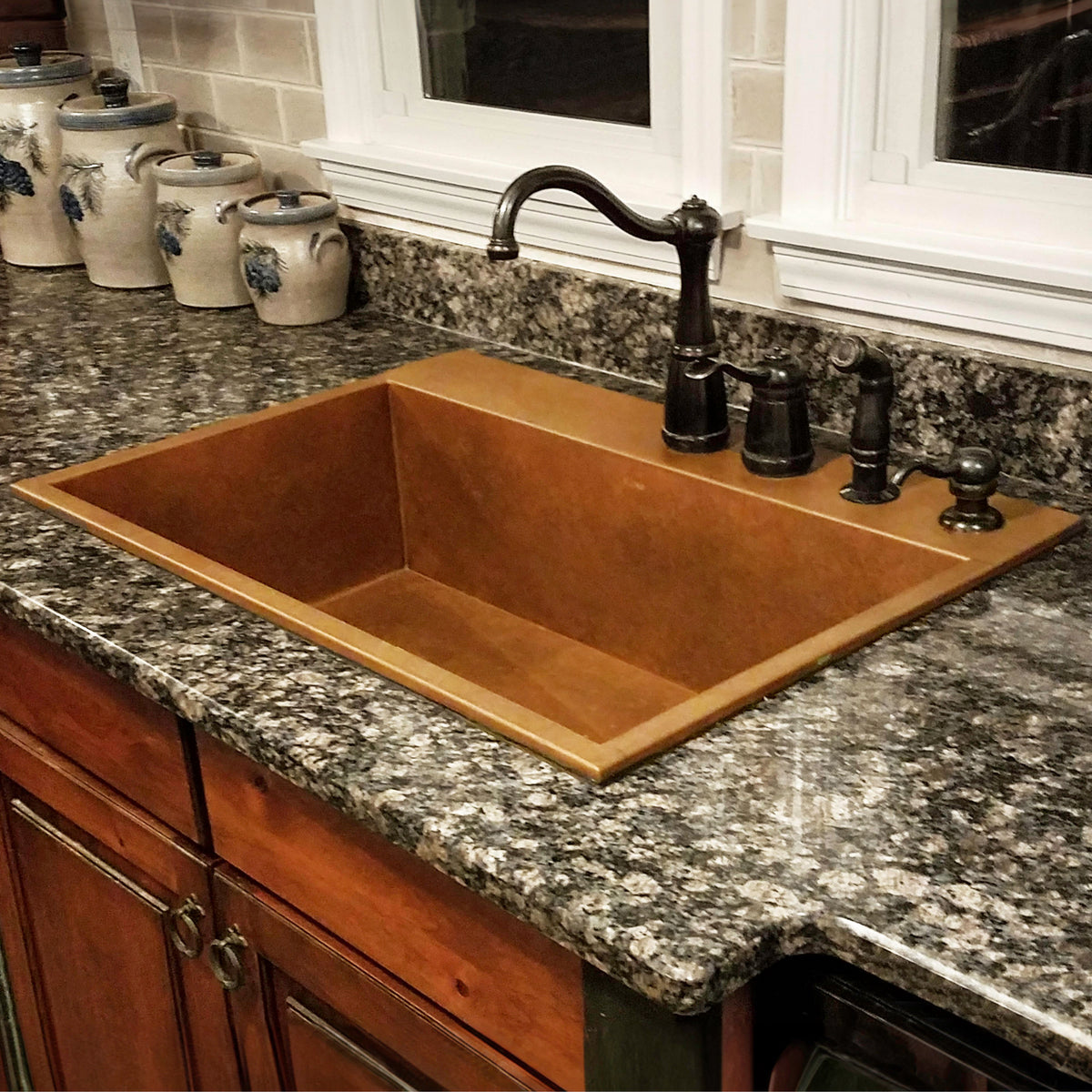 natural Copper undermount sink in dark granite countertop above cherry wood cabinets