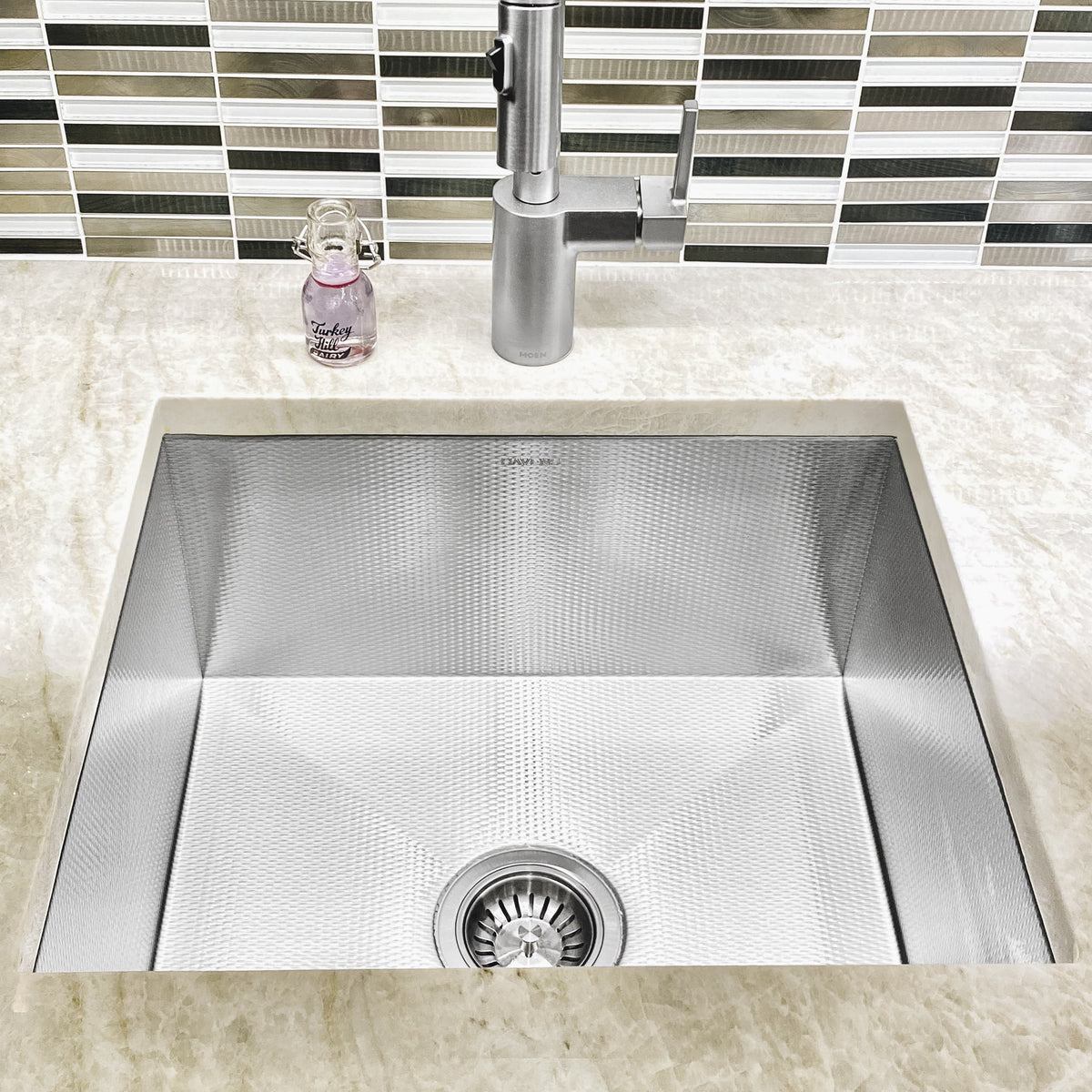 Textured prestige stainless steel undermount sink below a black and white mosaic tile backsplash