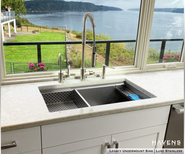 Undermount legacy advanced ledge stainless sink with drop in strainer and sponge caddy accesories overlooking a bay with mountains off in the distance 