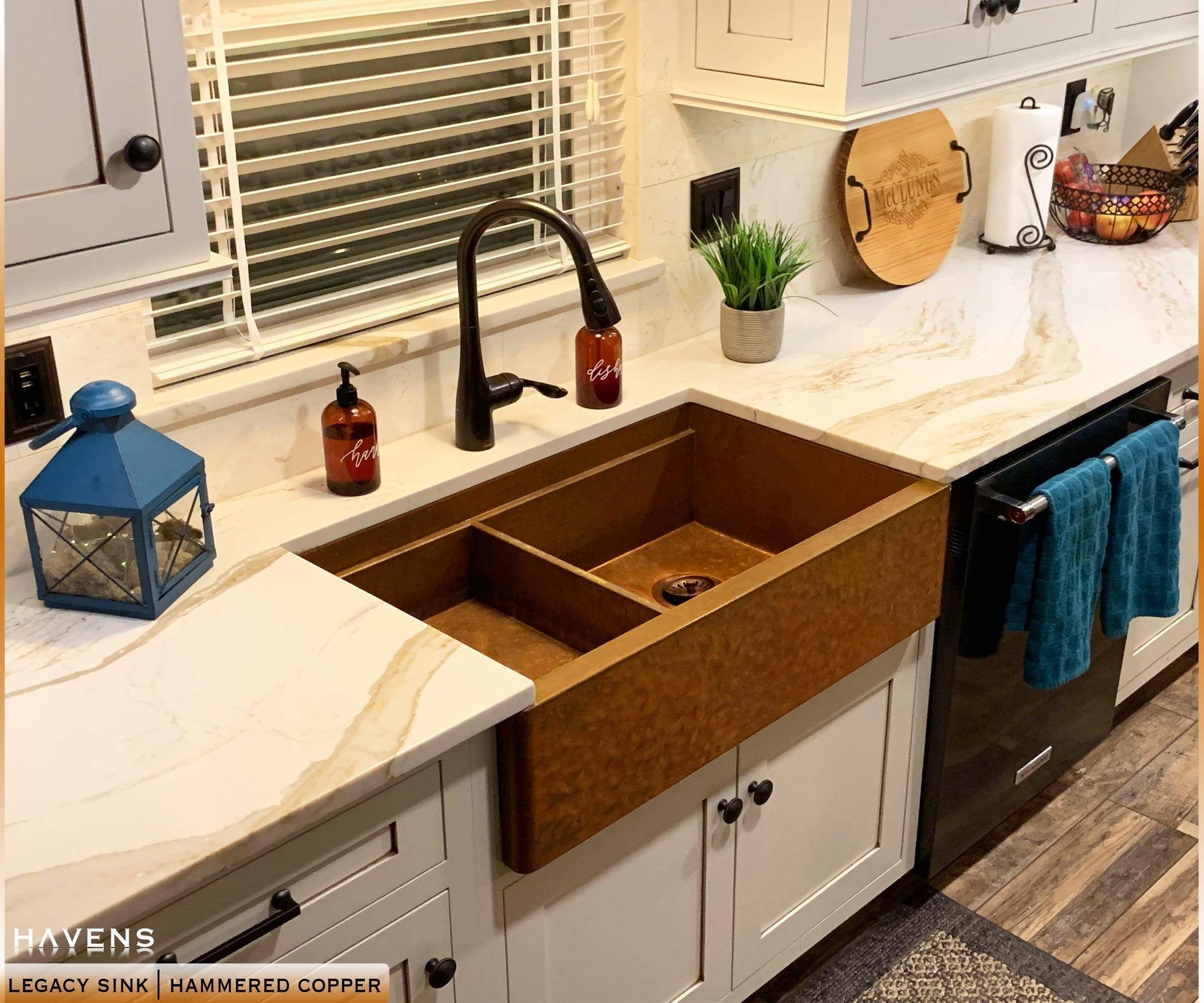 white farmhouse kitchen with drop in bowl placed on left side of hammered copper workstation sink 