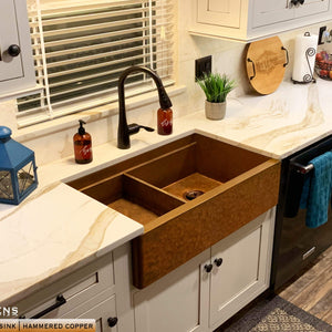 white farmhouse kitchen with drop in bowl placed on left side of hammered copper workstation sink 