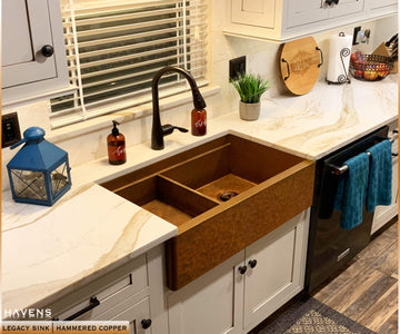 white farmhouse kitchen with drop in bowl placed on left side of hammered copper workstation sink 